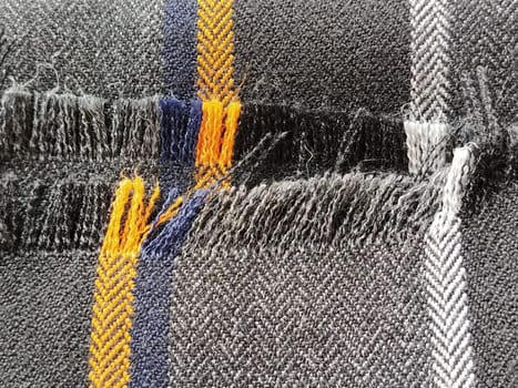 Light black-gray folded fabric with orange and dark blue stripes. Ripped, unfinished fabric edge. Interior decoration. Dress fabrics in casual style. Dense material for furniture finishing.