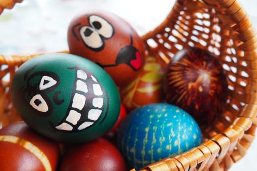 Easter eggs painted in different colors with painted laughing faces. Funny grimaces with eyes tongue and big white teeth. Scary face for Halloween. Emoticon for Easter Wicker basket. White background