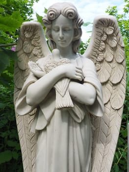 An angel with a dove. Sculpture in the cemetery. The figure of an angel with wings holding a bird in his arms. Lamentation for the deceased. Headstone monument on a Christian grave. Sadness sorrow