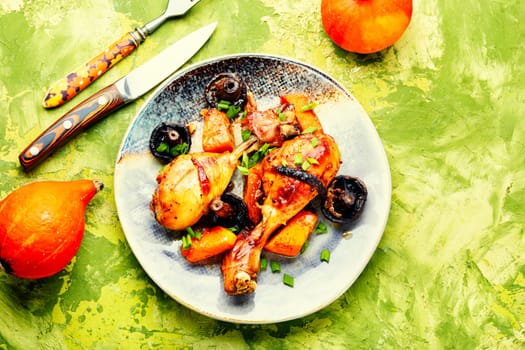 Chicken legs roasted with pumpkin on a table decorated with squash