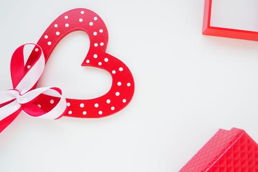 Valentine's day concept. Red wooden heart with white dots and a ribbon bow on a stick. Red gift box and photo frame. White background. Flat lay. Copy space.