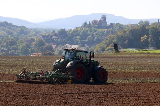 Landwirt eggt das Feld, im Hintergrund Burg Trendelburg, Hessen, Deutschland