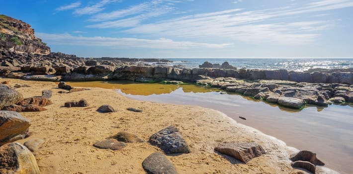 Pool of salt water on the rocky Headland at Point Arkwright with cloudy sky and a sunlit ocean.