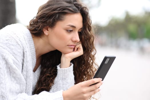 Serious woman using smart phone sitting in the street