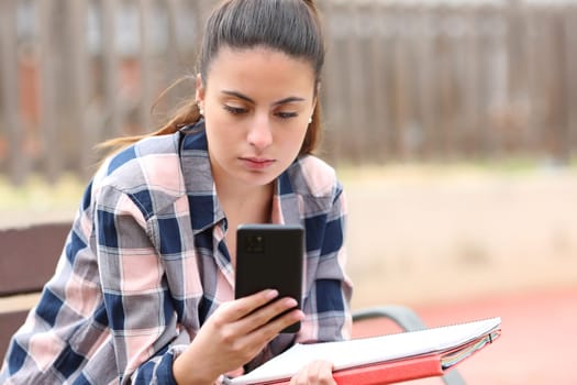 Student checking smart phone sitting in a park