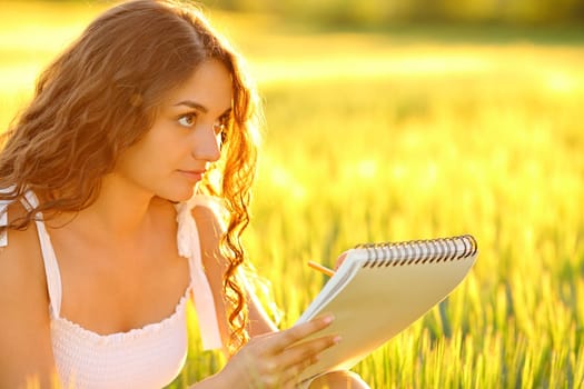 Woman drawing on notebook in a field at sunset