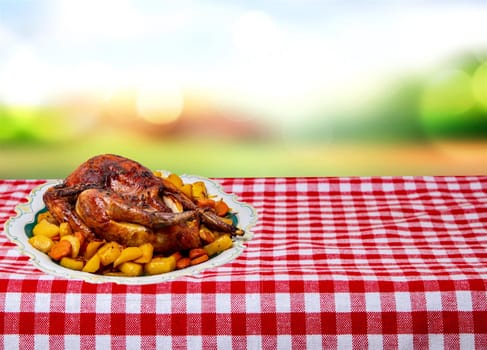 Grilled whole guinea fowl or baked pearl chicken on roasted potatoes and vegetables and port wine sauce is served on a beautiful plate on table over abstract natural background.