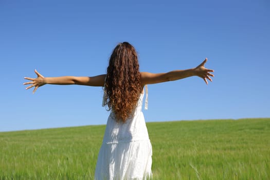 Back view portrait of a woman with white dress celebrating outstretching arms in a field