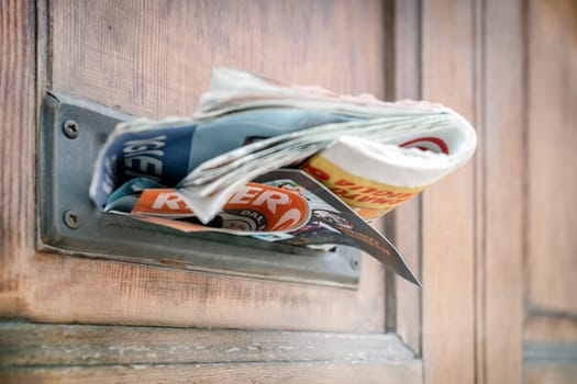 Many advertising leaflets are hanging from an overloaded letterbox. Closeup.
