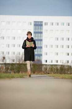 frontal full-body view of a mature woman in black leather jacket reading a book to the camera to go in front of white fuzzy plate construction in the background