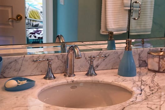 Detail of marble bathroom sink surrounded by blue walls and decor.