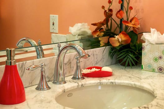 Detail of marble bathroom sink surrounded by orange walls and decor.