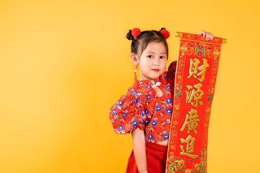 Chinese New Year. Happy Asian Chinese little child girl smile wearing red cheongsam qipao Spring festival couplets Character FU means fortune, blessing, studio shot isolated on yellow background