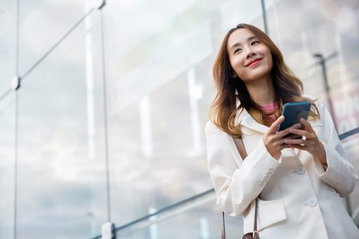 Portrait successful business woman smiling holding smartphone use application chat online in morning, Asian businesswoman working with mobile phone standing against street front building near office