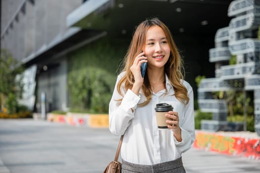 Beautiful woman walking outside in street and calling talking on mobile phone outdoors near office, portrait lifestyle businesswoman with bag cell to customer while holding coffee paper cup takeaway