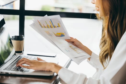 Freelance female hold paperwork documents paper graphs and using laptop at cafe, Asian young business woman working analyzing financial for budget or report graph document paper with computer