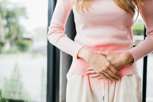 Asian young female unhappy unwell sick ill hand holding on stomach suffers pain at home, Sad Woman Stomach Ache from menstruation, Abdomen bloating and Chronic gastritis concept