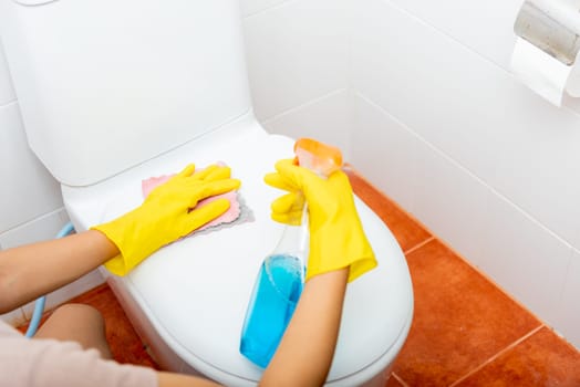 Woman cleaning toilet seat using liquid spray and pink cloth wipe restroom at house, female wearing yellow rubber gloves she sitting and wash cleaner bowl bathroom wc, Housekeeper healthcare concept