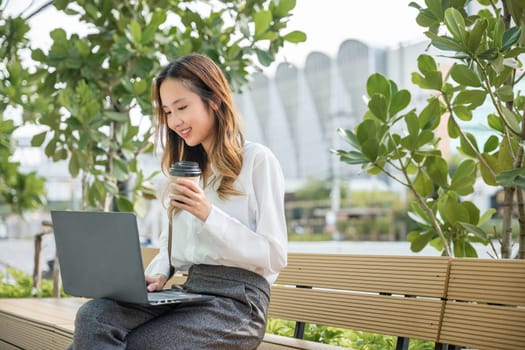 Successful Asian business young woman working laptop outdoor corporate building exterior, Happy professional smiling businesswoman sitting alone typing computer outside street city near office
