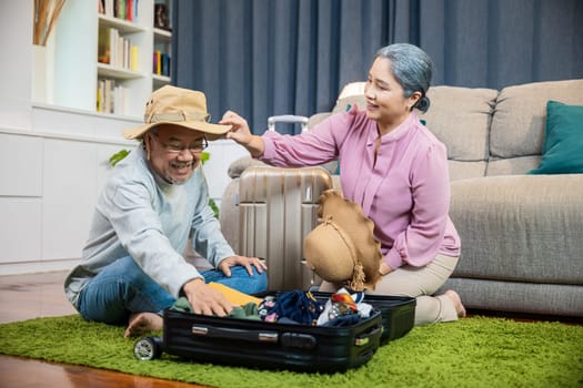 Asian couple old senior marry retired prepare luggage suitcase arranging for travel, Romantic retired couple packing clothes travel bag suitcase together on floor at home interior living room