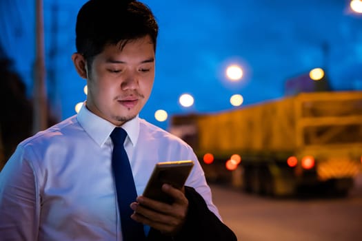 Young man walking and chatting on mobile phone with friends at social networks outdoor, Portrait Asian businessman typing an sms message via smartphone after work near office at night city street