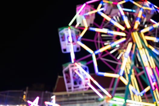 Blurry rollercoaster in bokeh, Ferris wheel at night of colorful with outdoor, Defocused blurred and blur image of Amusement park, The annual temple event has activities. Image out of focus