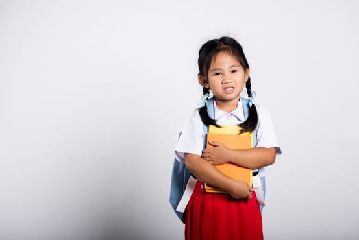 Asian adorable toddler smiling happy wear student thai uniform red skirt stand hold or hugging book in studio shot isolated on white background, Portrait little children girl preschool, Back to school