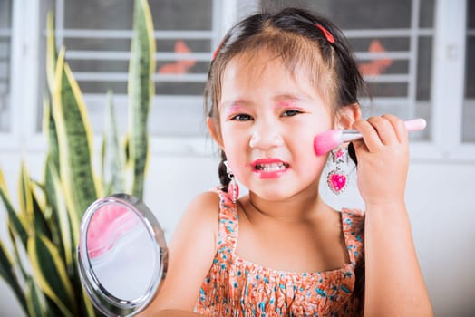 Happy kid is beautiful make up with cosmetics toy, Asian adorable funny little girl making makeup her face she looking in the mirror and cheek fluffy brush for powder, Learning activity to be woman