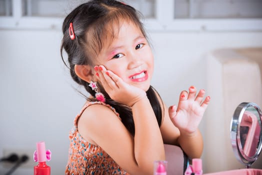 Closeup of happy kid is beautiful make up face with cosmetics toy, Asian adorable funny little girl making makeup her face, Learning activity to be woman, fashion beauty children at home
