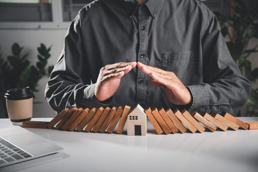 Business risk plan real estate protection. Man hand blocks wood block from many row falling wooden block like domino to house model, Insurance ideas to prevent loss concept