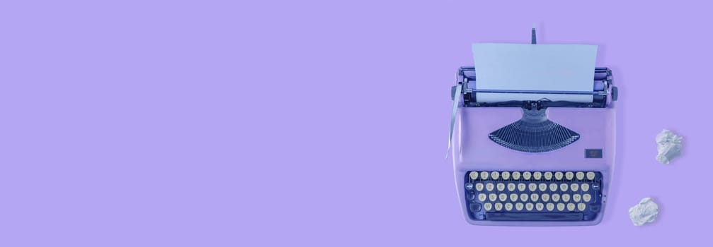 A violet vintage typewriter with violet background and two paper balls.