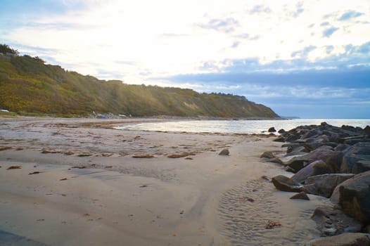 Sunset on the Danish coast. Beach, waves. Hill with trees in background. Landscape photo from sea