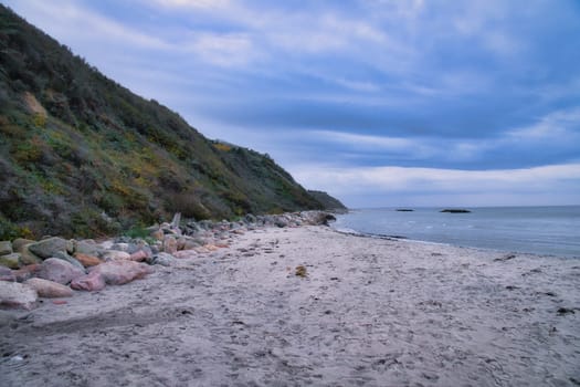Sunset on the Danish coast. Beach, waves. Hill with trees in background. Landscape photo from sea