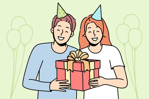 Guy, girl in party hats are smiling, holding gift box tied with ribbon. Meeting guests at holiday. Celebrating birthday, anniversary, significant event. Vector line art multicolored illustration.
