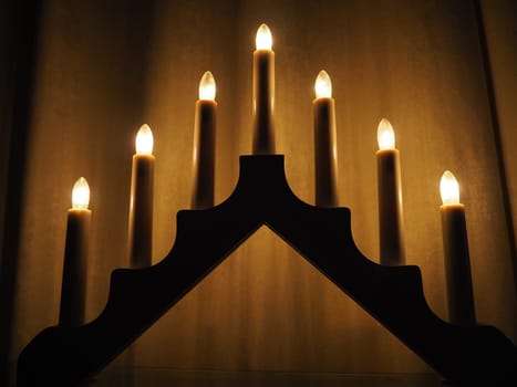 Schwibbogen arch luminaire in the form of a triangular candlestick. Yellow background. Evening, romantic, festive, religious or mystical atmosphere. Burning light bulbs that resemble candlelight.