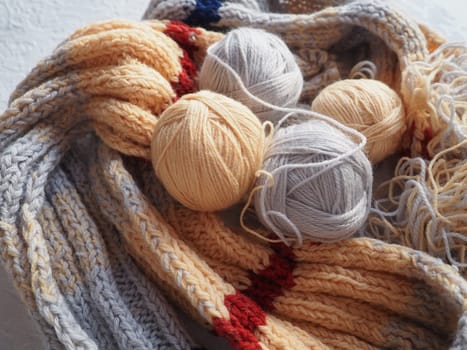 Knitting a scarf or sweater from gray, beige and orange yarns. Balls of woolen and acrylic threads. Knitting as a hobby. Accessories, knitting needles, crochet hooks