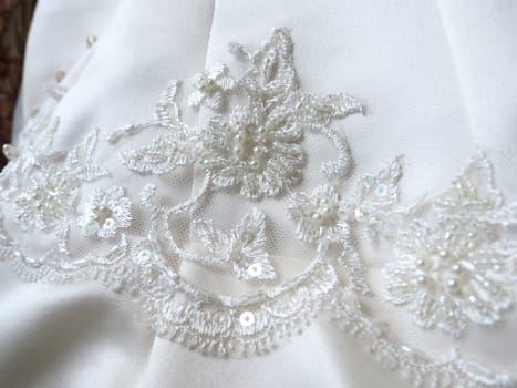 Beaded embroidery and lace close-up on a white wedding dress. Beautiful jewelry for the bride's outfit. Wedding preparations. Clothes of the newlyweds. Small shiny details on the dress, handmade.