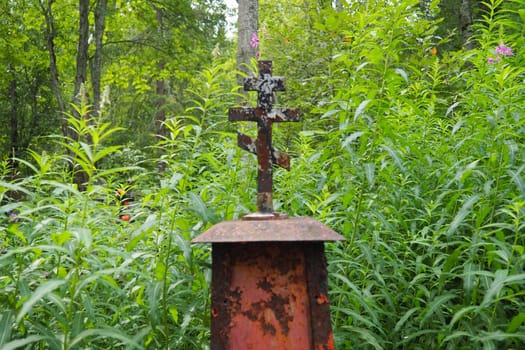 Metal cross on the grave. Monument in the form of a cross in the cemetery. Daytime in summer. The theme of grief, death and Halloween. Religious Christian symbol of the repose of the soul.