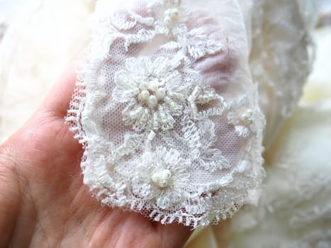 Hand touches beadwork and lace close-up on a white wedding dress. Beautiful jewelry for the bride's outfit. Wedding preparations. Clothes of the newlyweds. Small shiny details on the dress, handmade.