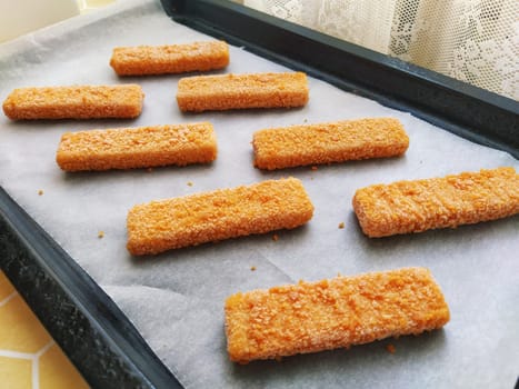 Frozen fish sticks are laid out on baking paper. Cooking a fish delicacy. Baking paper on a baking sheet. A quick lunch from the oven. Fish menu. Healthy protein food. Low-calorie diet.
