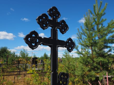 Metal cross on the grave. Monument in the form of a cross in the cemetery. Daytime in summer. The theme of grief, death and Halloween. Religious Christian symbol of the repose of the soul.