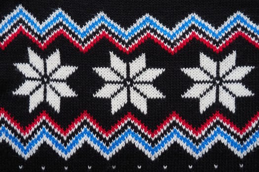 Jacquard knitted pattern. Geometric ornament for Christmas or New Year. Knitted white snowflakes, blue zigzag, dots on a black background. Winter fashionable modern vegetable traditional folk ornament