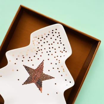 A plate in the shape of a Christmas tree with gold ornaments and a star in the middle. Gift wrapping. Green background. New Year Christmas card. Background for advertising and lettering. Copy space