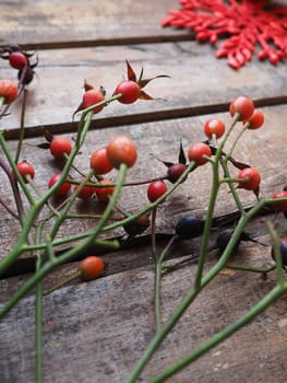 Red fruits of wild rose or rose bush on a wooden background. Red carved star with sequins on the back backdrop. Autumn, New Year or Christmas still life.