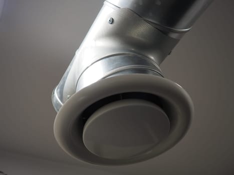 Extractor hood in a public toilet. Round metal pipe with gray air extractor. Engineering ventilation systems. Galvanized pipes under the ceiling of the room. Plastic round tip.