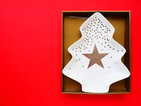 A plate in the shape of a Christmas tree with gold ornaments and a star in the middle. Gift wrapping. Red background. New Year Christmas card. Backdrop for advertising and lettering. Copy space
