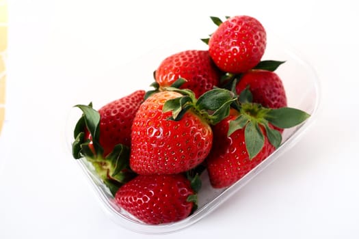 Ripe strawberries in a plastic package on a white background. Delicious fresh berries in a container for sale to customers. Keeping food fresh. Healthy food, vitamins and microelements