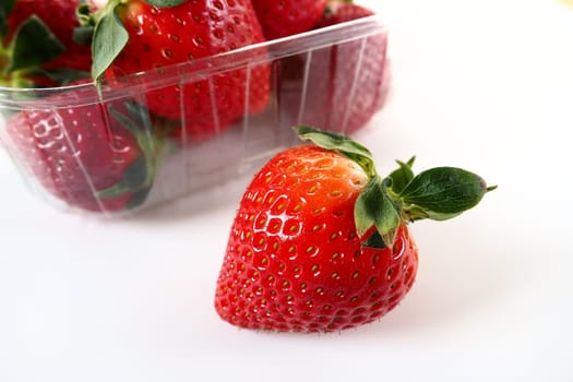 Ripe strawberries in a plastic package on a white background. Delicious fresh berries in a container for sale to customers. Keeping food fresh. Healthy food. One strawberry pulled out of the container