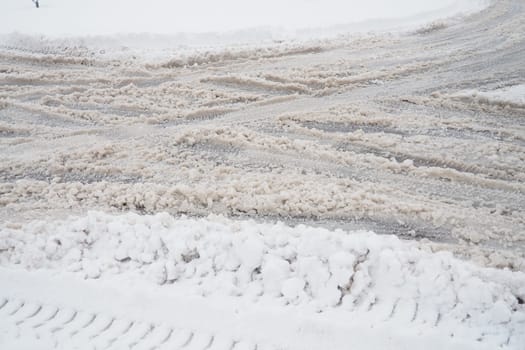 A fork or siding from a roundabout. Snowdrifts on the side of the road. Bad weather and traffic. Snow on the asphalt. Difficult driving conditions. Winter slush on the auto path