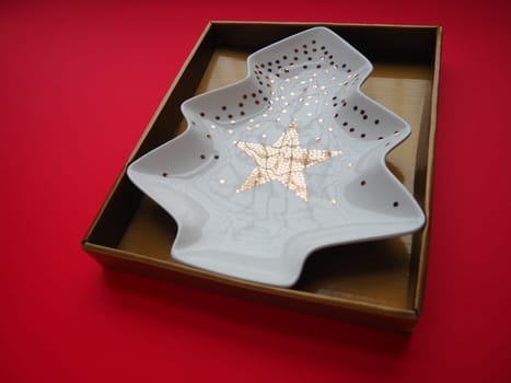 A plate in the shape of a Christmas tree with gold ornaments and a star in the middle. Gift wrapping. Red background. New Year Christmas card. Backdrop for advertising and lettering. Copy space